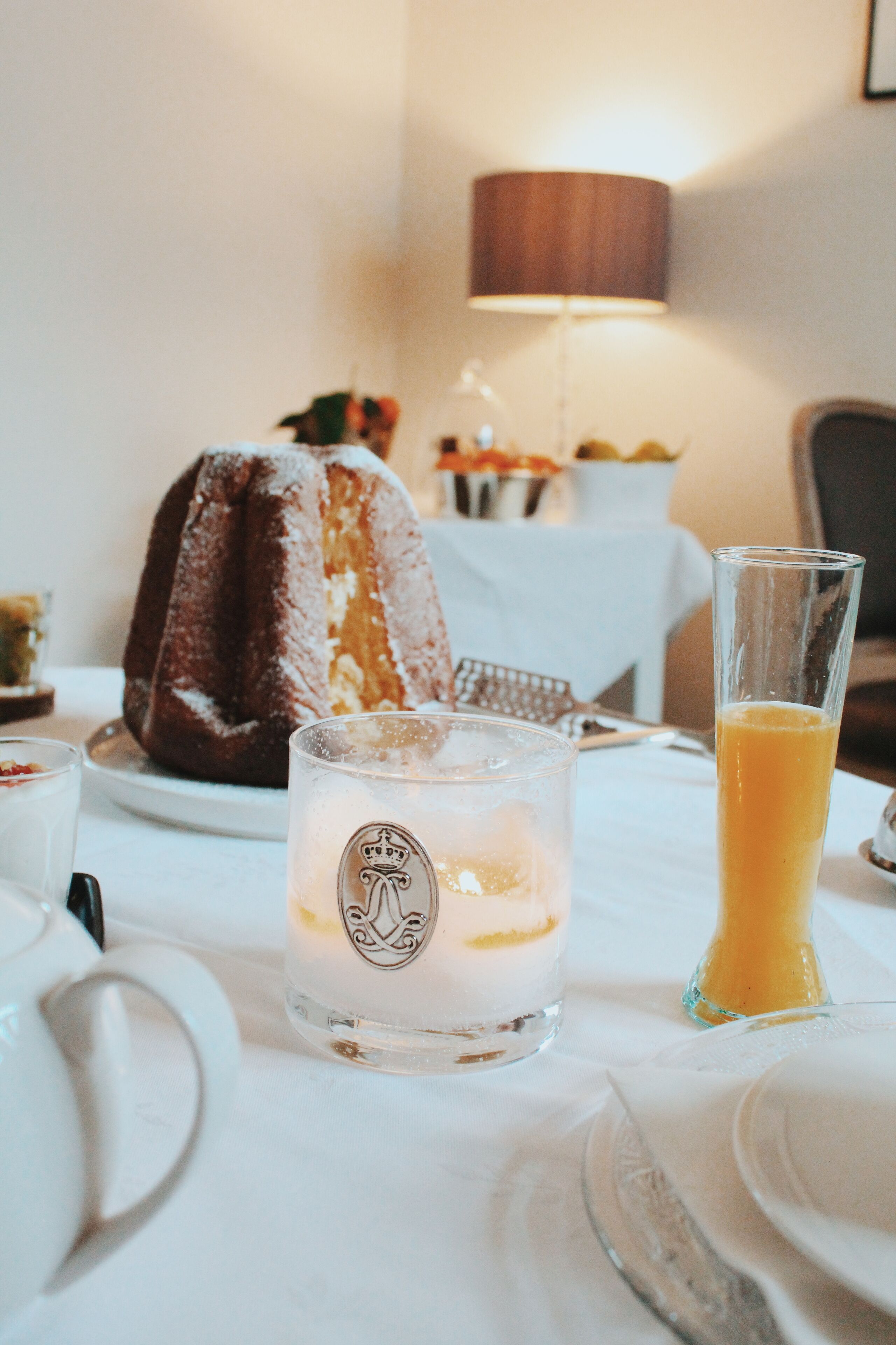 Una mesa de comedor con un pastel bundt, un vaso de jugo de naranja y una vela.