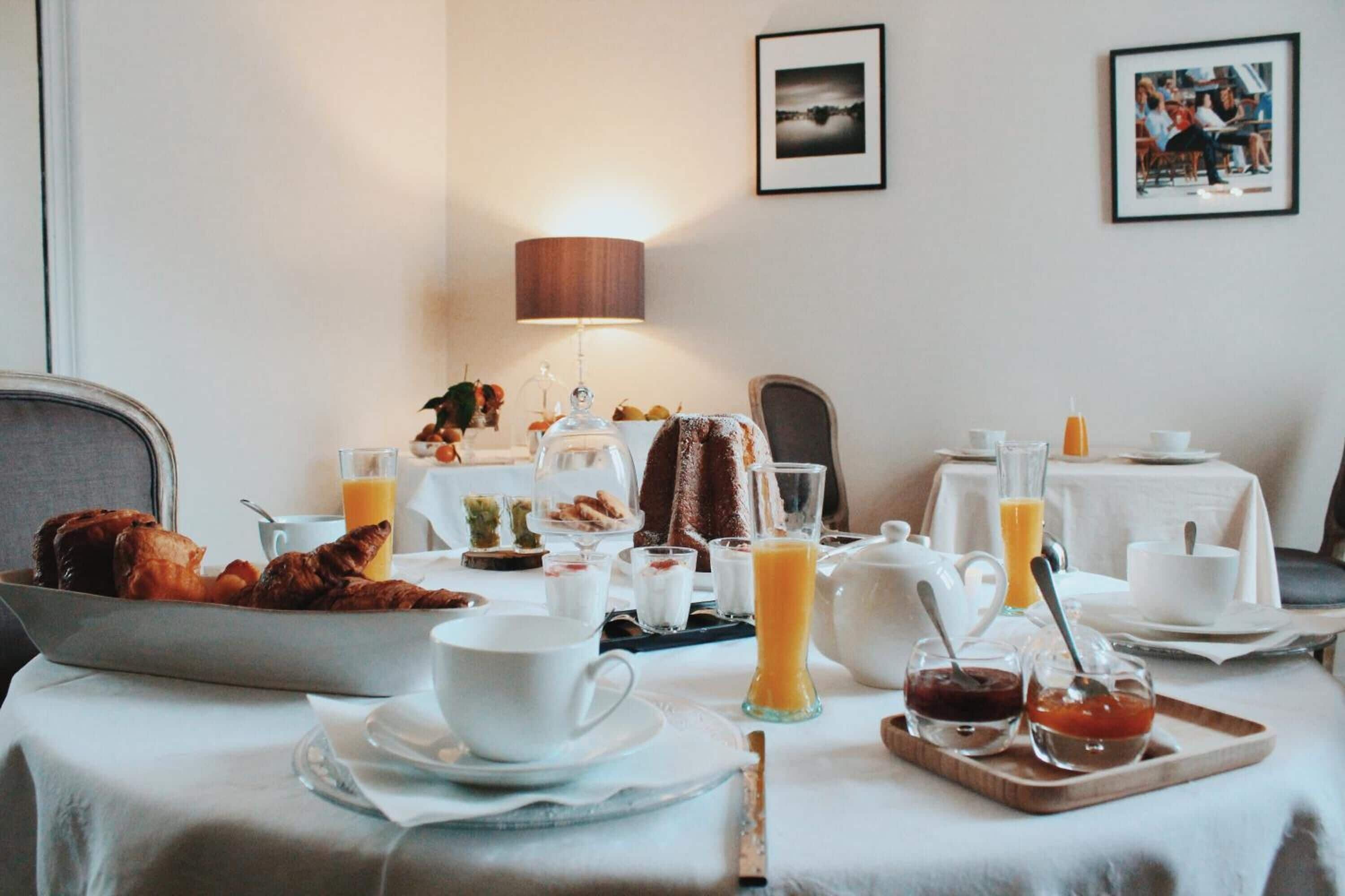 Een ontbijt met verschillende soorten eten, zoals gebak, fruit en drankjes, gepresenteerd op een tafel met een lamp en foto's in de muur.