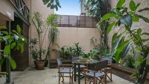 A patio area with a round table and chairs, surrounded by potted plants and a brick wall. - Family Terrace Home Close to Oxford Street and CBD (Darlinghurst)