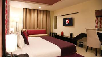 A hotel room with a bed, a desk, a chair, a TV, and a lamp.