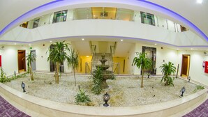 A spacious indoor atrium with a central fountain, surrounded by potted plants, and a second-floor balcony with glass railings. - Swiss Spirit Hotel & Suites Taif (Taif)