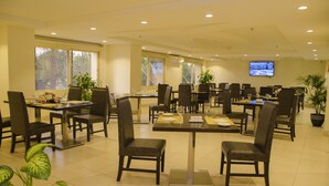 A spacious dining area with multiple tables and chairs, large windows, and a television screen on the wall. - Swiss Spirit Hotel & Suites Taif (Taif)