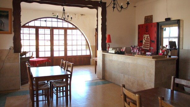 Un coin repas avec une table et des chaises en bois, une nappe rouge, et un espace cuisine avec un comptoir rouge et divers objets disposés dessus.