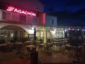 Un espacio al aire libre con mesas, sillas, un bar y el letrero de un restaurante.
