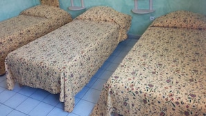 Une chambre avec trois lits, chacun recouvert d’une couette à motifs floraux. Deux petites tables avec des chaises sont placées contre le mur.