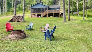 A cabin with a deck and a fire pit area with Adirondack chairs. - Blessed on the New River - Riverfront, WIFI, Small Dog Friendly, Firepit, Gas Grill, Gas Stove (Lansing)