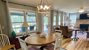 A dining area with a round wooden table, white chairs, and a chandelier. - Blessed on the New River - Riverfront, WIFI, Small Dog Friendly, Firepit, Gas Grill, Gas Stove (Lansing)