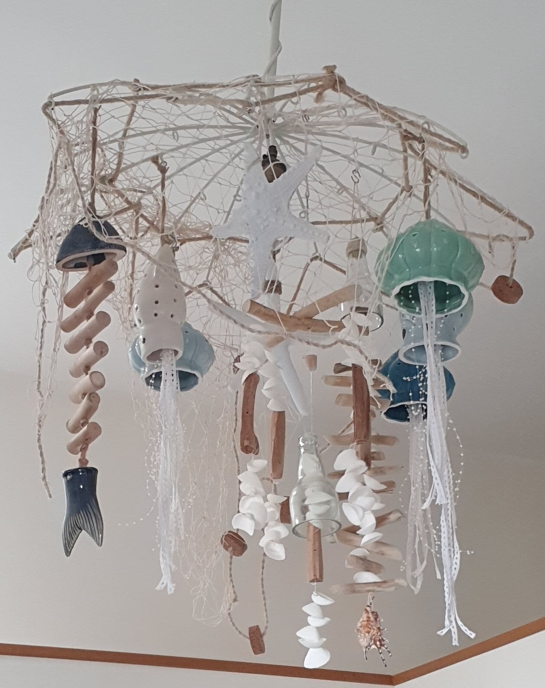 Ein dekoratives Hängeobjekt mit verschiedenen Formen und Materialien, darunter Muscheln, Perlen und Stoffelemente.