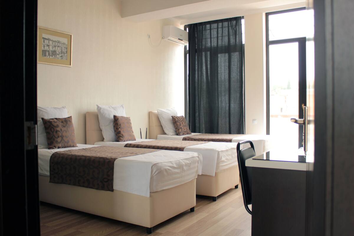 A hotel room with two beds, a desk, and a window with curtains.