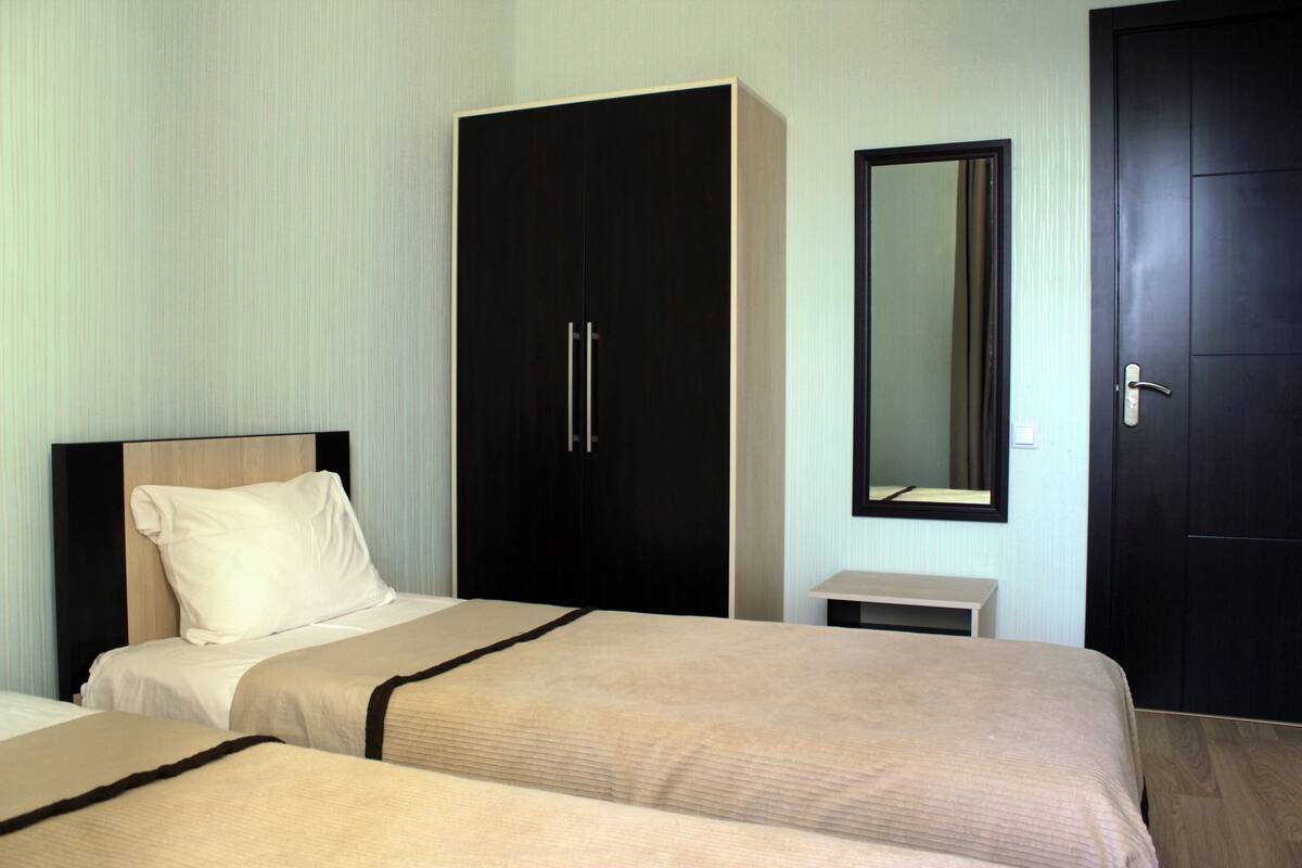 A hotel room with two beds, a wardrobe, a mirror, and a door.