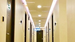 A long, narrow hotel corridor with doors on both sides, illuminated by overhead lights, and a green directional sign on the left wall. - Two Seasons Executive Suites (Zamboanga)