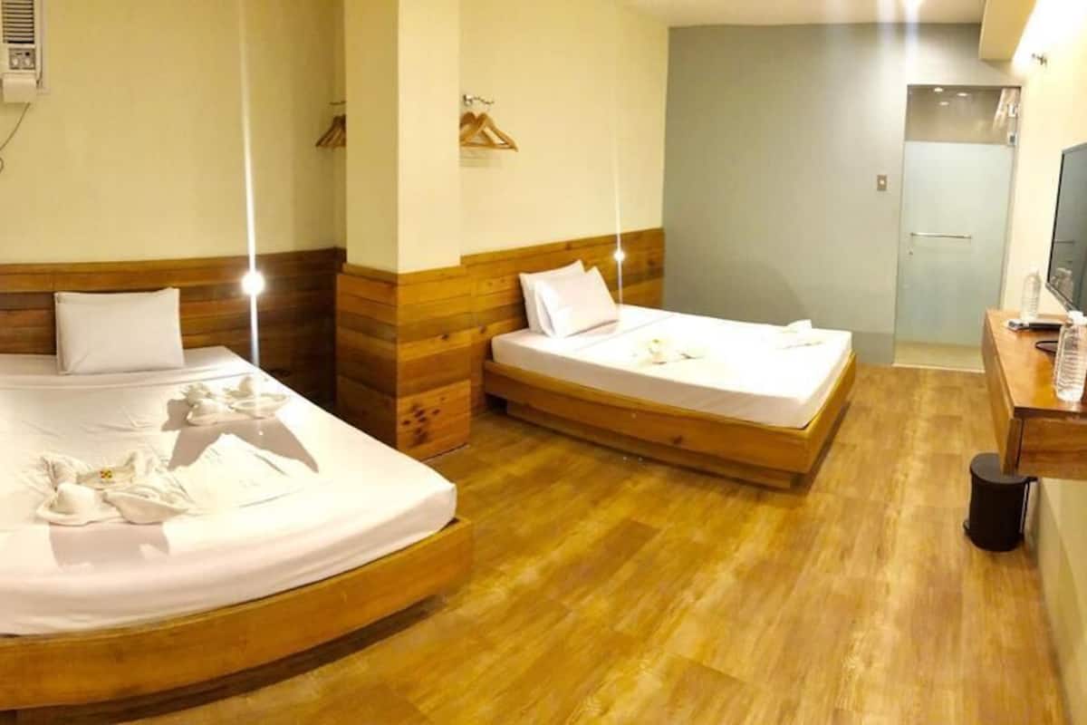 A hotel room with two beds, wooden headboards, a TV, and a shower area.