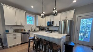Una cocina moderna con armarios blancos, electrodomésticos de acero inoxidable, una isla grande con taburetes y vistas por la puerta.