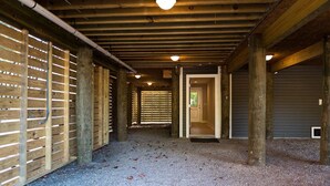 Un espacio al aire libre cubierto, con suelo de grava, paredes de listones de madera y una puerta central que da a un espacio interior.