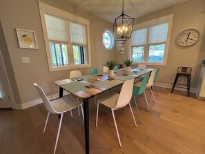 A dining area with a long table, chairs, a hanging light fixture, and a clock on the wall.