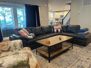 A living room with a sectional sofa, a coffee table, and a view of the kitchen.