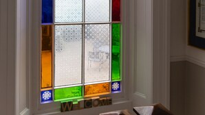 Une fenêtre en vitrail avec une inscription « BIENVENUE » en dessous, des murs recouverts de panneaux blancs et un luminaire suspendu.