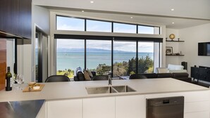 A modern kitchen with a large island, a dishwasher, and a view of the ocean. - Wakatu View - Nelson Luxury Holiday Home (Atawhai)