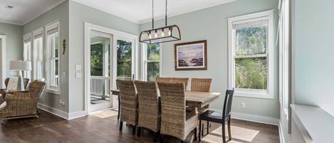 A dining area with a table and chairs, a hanging light fixture, and a window with a view of greenery.