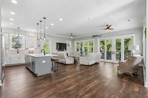 A spacious living area with a kitchen, dining space, and a balcony with large windows. - High Tides| Walk to Beach & Center St| Rooftop Deck| Porches| Spacious Living| Seasonal Hot Tub (Folly Beach)
