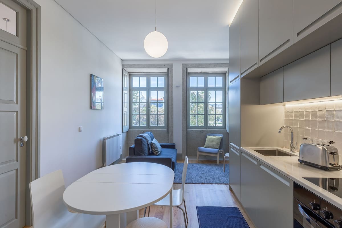 A compact kitchen with a dining area, large windows, and a modern light fixture.