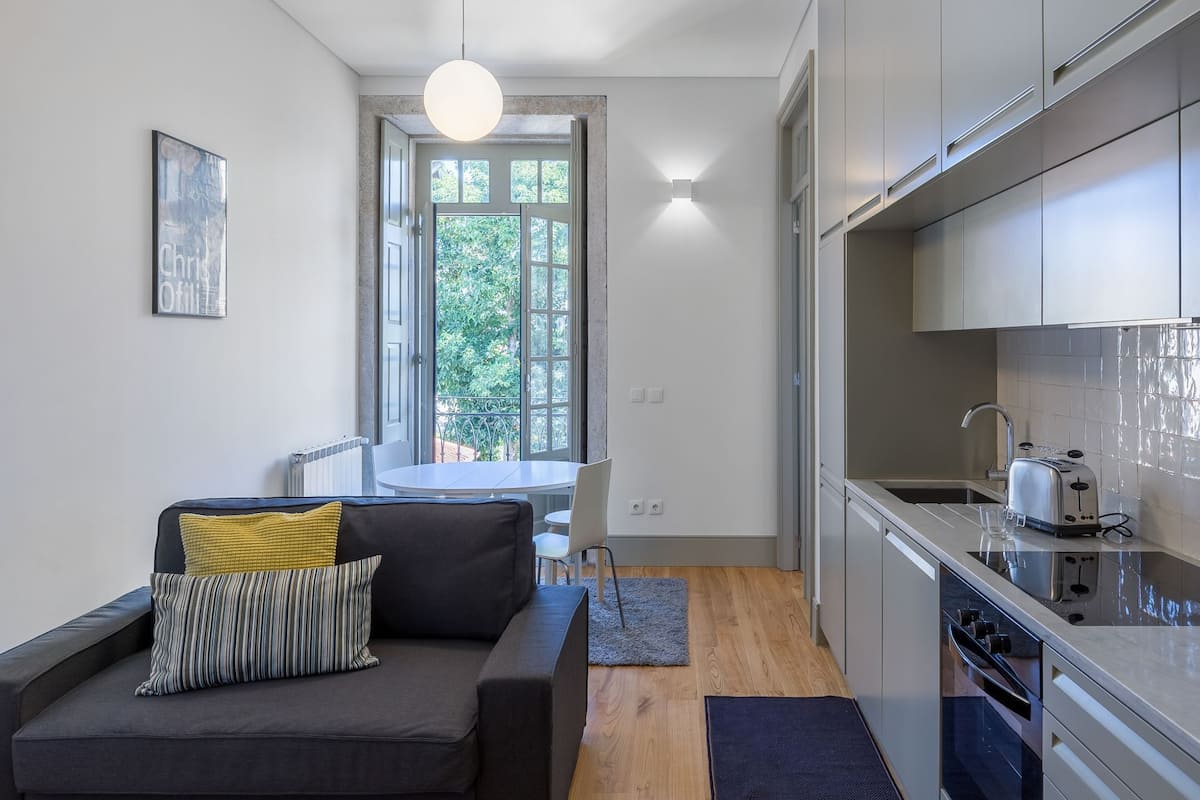 A modern apartment with a living area featuring a sofa, a dining table, and a kitchen with a sink and stove.