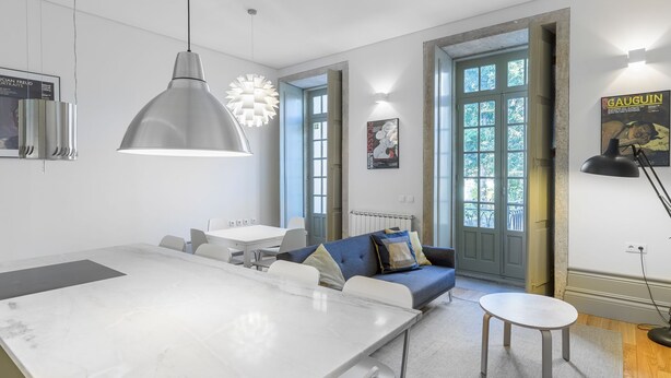 A modern kitchen with a marble countertop, pendant lighting, and a dining area with a sofa and a small table. - Casa Amarela (Porto)