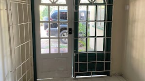 A room with a white tiled floor, a black doormat, and a door with a green frame and white panels. - Widcombe House (Kingston)