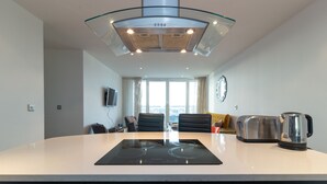 A modern kitchen with a central island, a built-in stove, and a glass-enclosed range hood. - Kenny Apartment  Austin David Apartments (London)