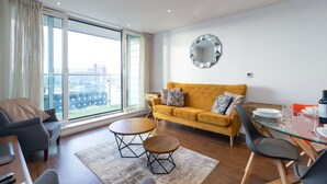 A modern living room with a sofa, two coffee tables, and a dining table set for four. - Kenny Apartment  Austin David Apartments (London)