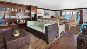 Un salon chaleureux avec un canapé, une bibliothèque, un coin repas et une vue sur la mer.