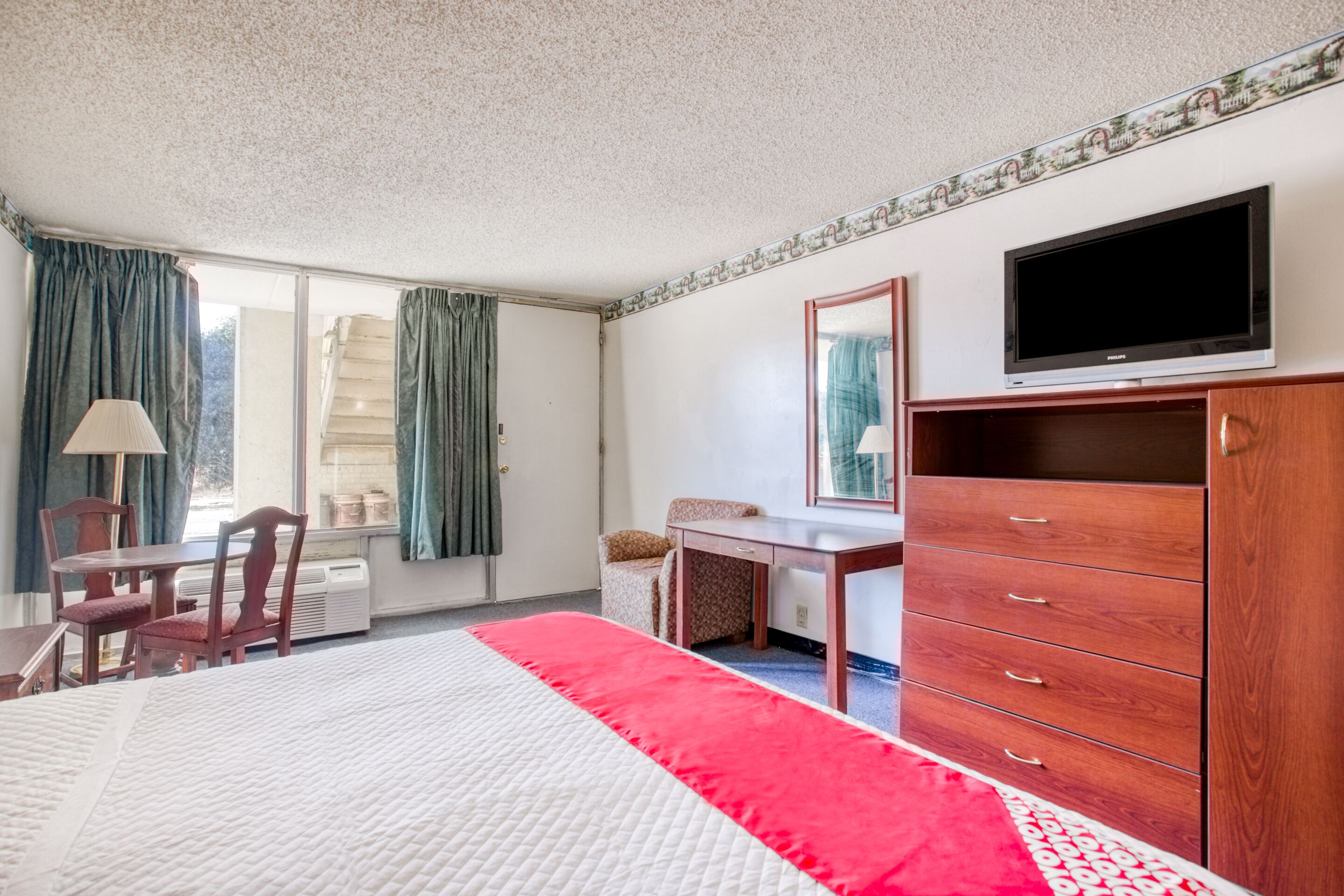 A hotel room with a bed, a desk, a chair, a dresser, and a television.
