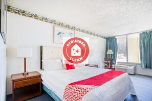 A clean hotel room with a bed, bedside table, lamp, and a window with curtains. -  Travelers Inn By OYO, Templeton VA (Petersburg)