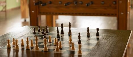 A chessboard with pieces set up in the foreground, with a wooden table and a foosball table in the background.