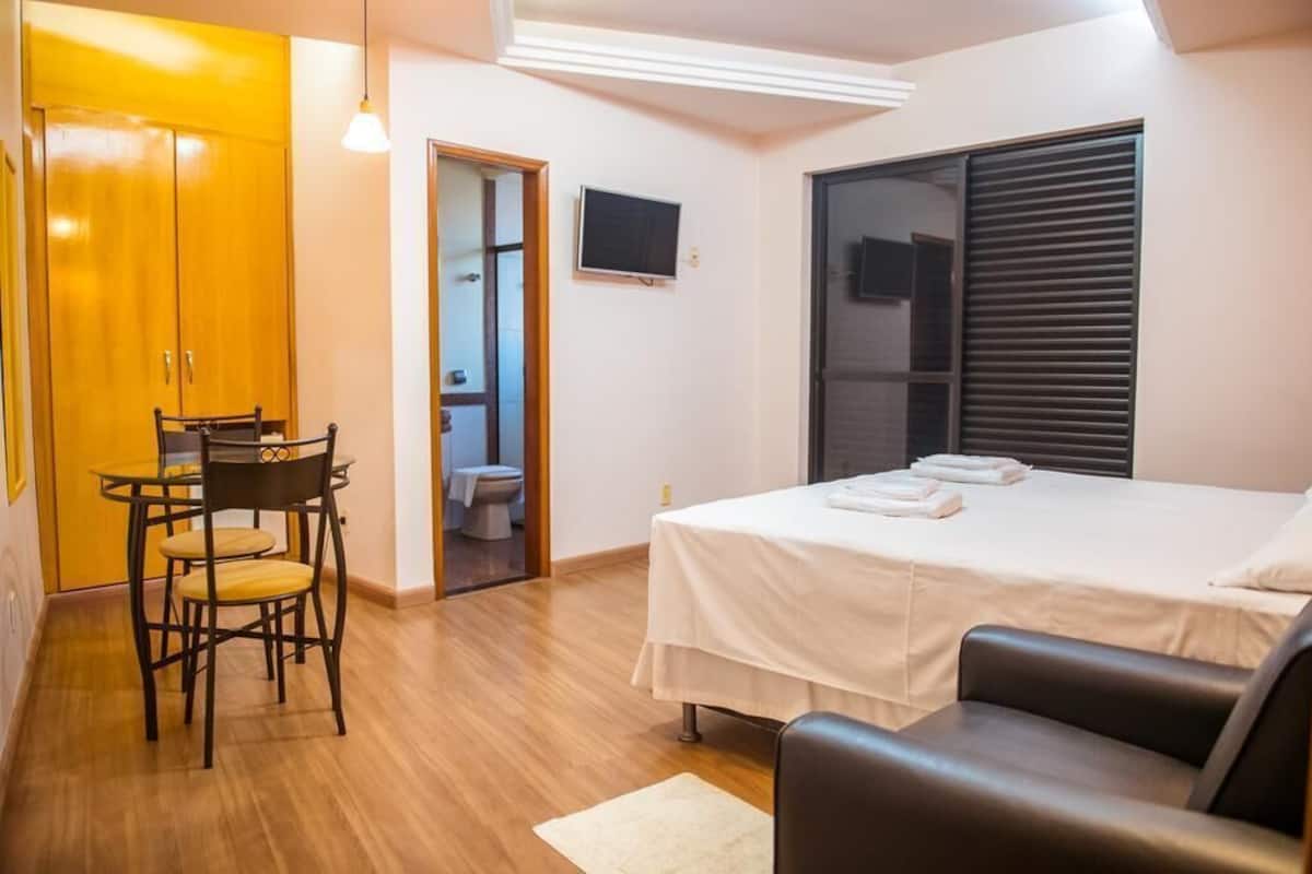 Ein Schlafzimmer mit Bett, Stuhl, Tisch, Fernseher und Fenster.