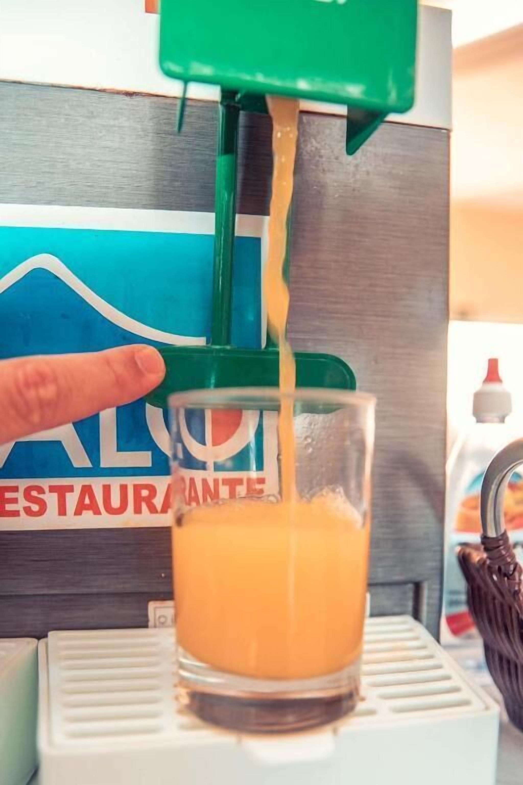 A hand pouring orange juice from a green dispenser into a clear glass.