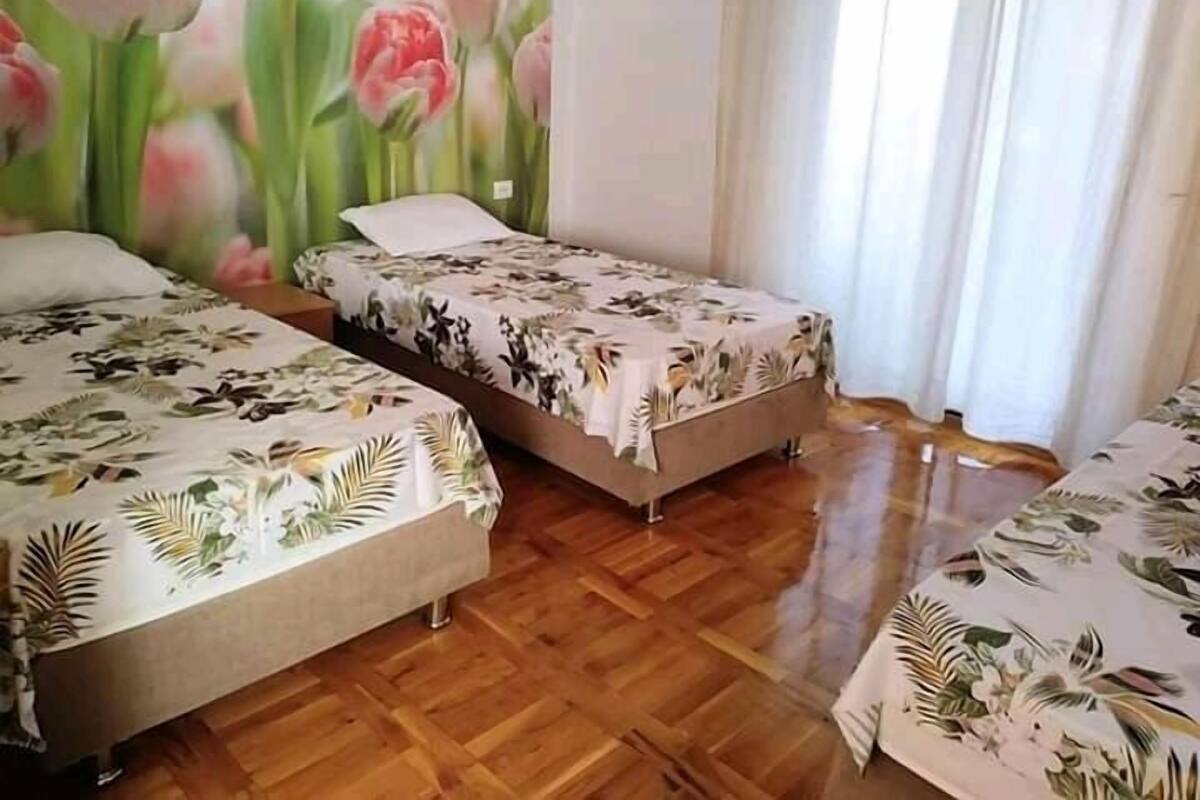 Una habitación con dos camas, cada una con una colcha estampada con flores, piso de madera y un gran mural floral en la pared.