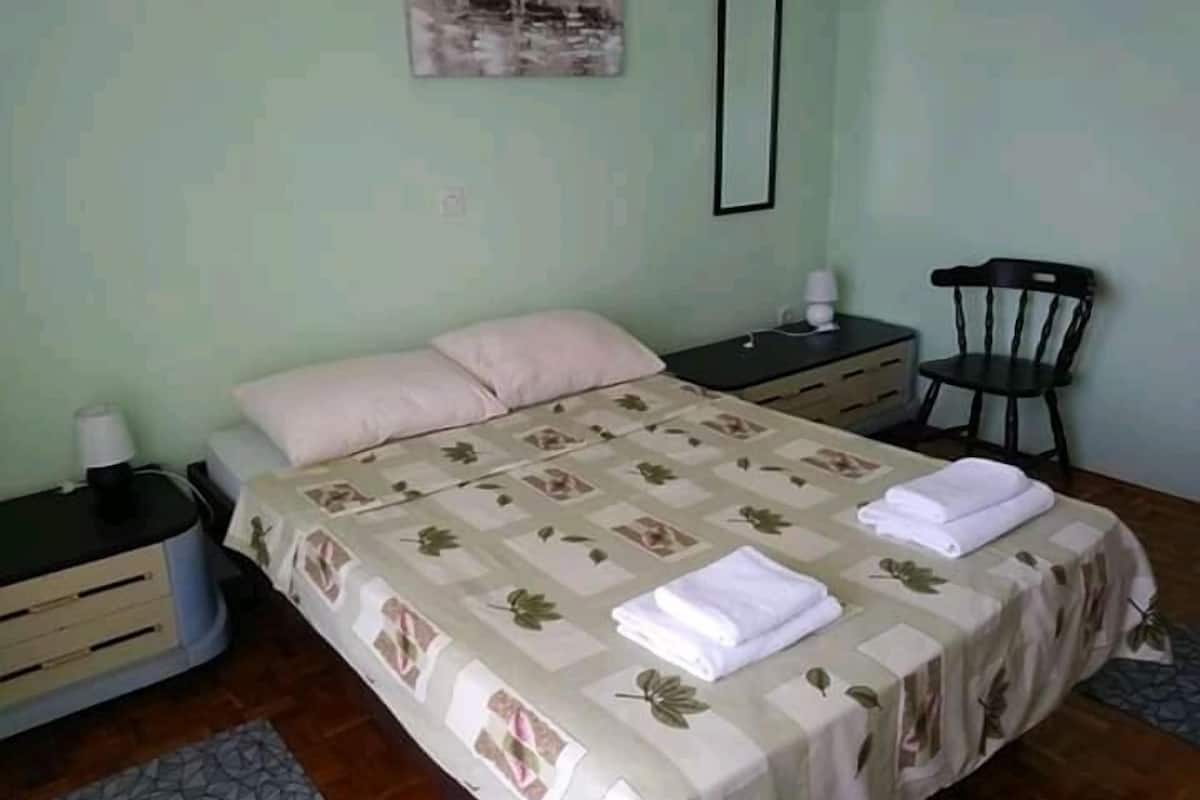 Un dormitorio ordenado con una cama, mesitas de noche, una silla y un cuadro en la pared.