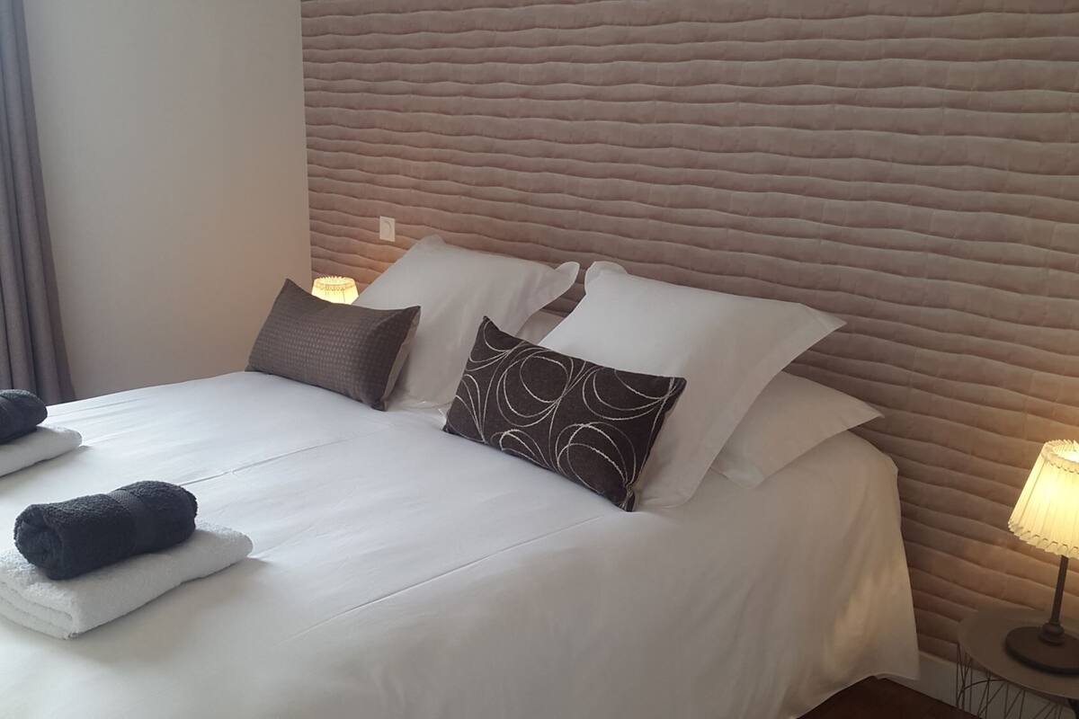 A neatly made bed with white linens and two rolled towels, a headboard with a textured pattern, and two bedside lamps.