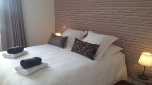 Un lit bien fait, avec du linge de lit blanc et deux serviettes enroulées, une tête de lit à motifs et deux lampes de chevet.