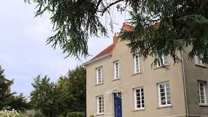 A two-story building with a blue door and white windows, surrounded by greenery. - Chambre d'Hotes La Maison du Parc (Les Epesses)
