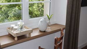 A wooden shelf with a tray holding glass jars and a white pitcher, a vase with a plant, and a window with a view of greenery. - Chambre d'Hotes La Maison du Parc (Les Epesses)