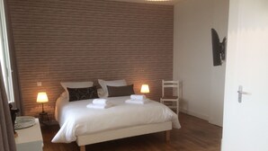 A neatly made bed with white linens and towels, two bedside lamps, a wooden floor, and a white chair. - Chambre d'Hotes La Maison du Parc (Les Epesses)