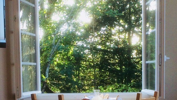 A breakfast table with bread, jam, and a pitcher of juice, set against a backdrop of trees and a window. - Chambre d'Hotes La Maison du Parc (Les Epesses)