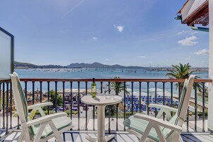 Un balcón con vista al mar, una mesa con dos vasos y una botella, y varias sillas.