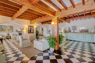 Amplia sala de estar con suelo a cuadros, vigas de madera, muebles blancos y plantas en macetas.