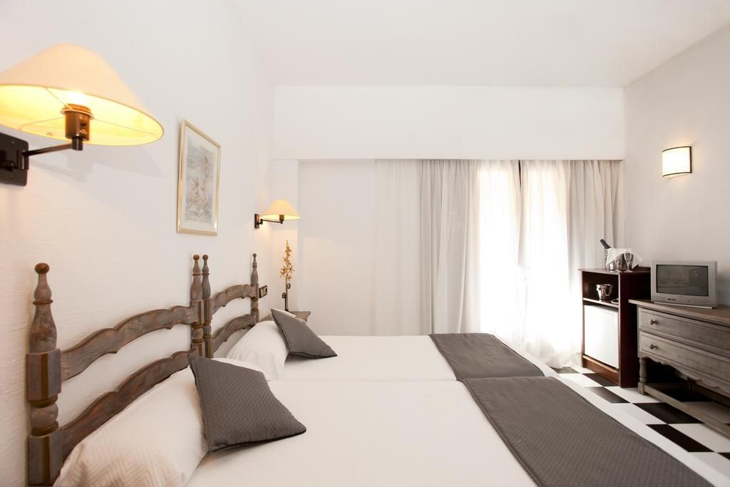 Habitación de hotel con una cama grande, dos lámparas de noche, un televisor y piso a cuadros.