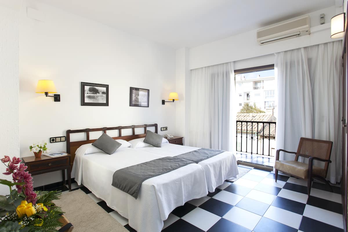 A hotel room with a large bed, two bedside tables, a chair, and a balcony with a view.