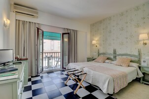 Una habitación de hotel con piso de cuadros, dos camas con almohadas a juego, un escritorio con computadora y un balcón con vista.