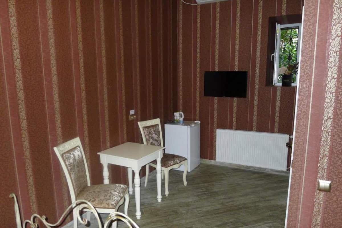 A room with striped wallpaper, a white radiator, a small table with two chairs, and a television mounted on the wall.